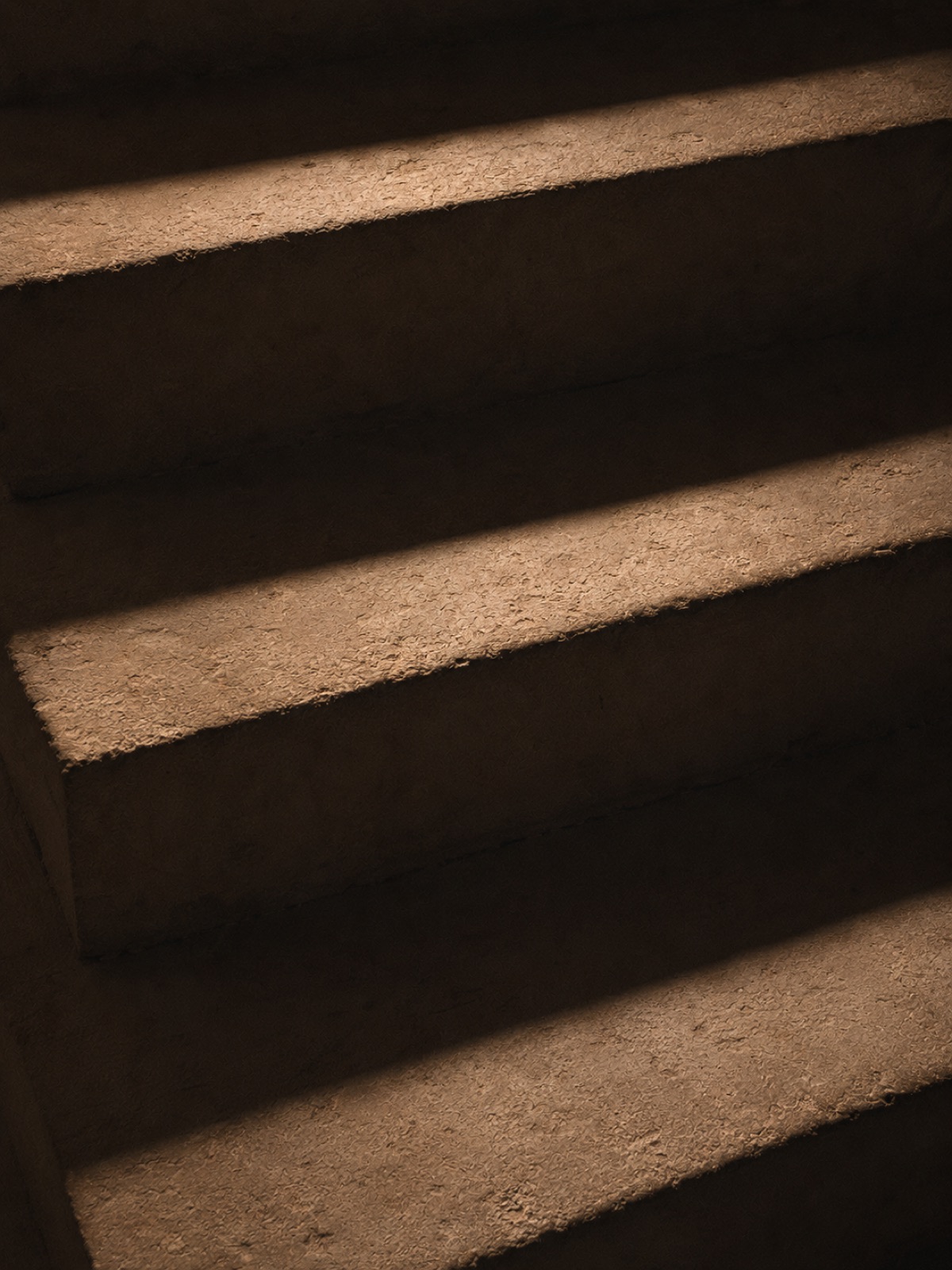 Escalier dans la pénombre, la lumière rasante révèle le grain de chaque marche